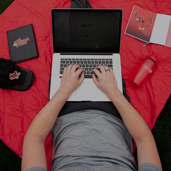 Student using a laptop computer sitting on a red blanket.